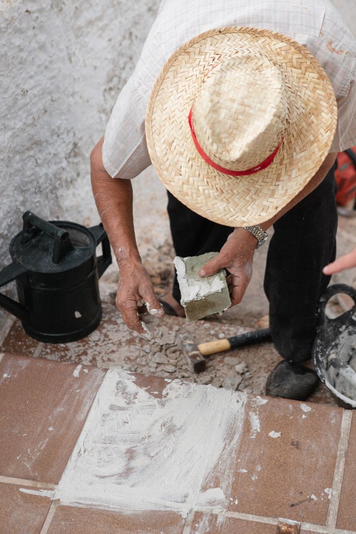 A man in a straw hat laying bricks outdoors in Ciutadella de Menorca, Spain.