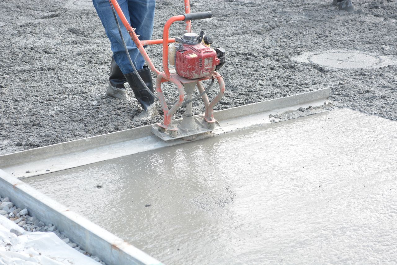 A construction worker operates a power trowel to smooth freshly poured concrete on a construction site.